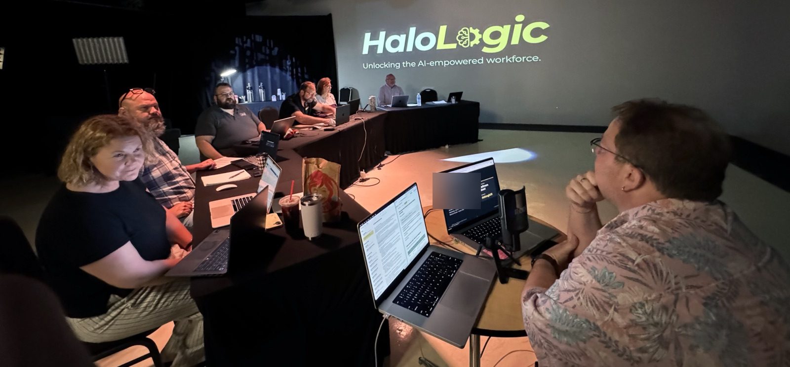 Brad Bear leads the session from a laptop and microphone while attendees smile from black-draped tables, the Halo Logic logo projected on the wall behind them.