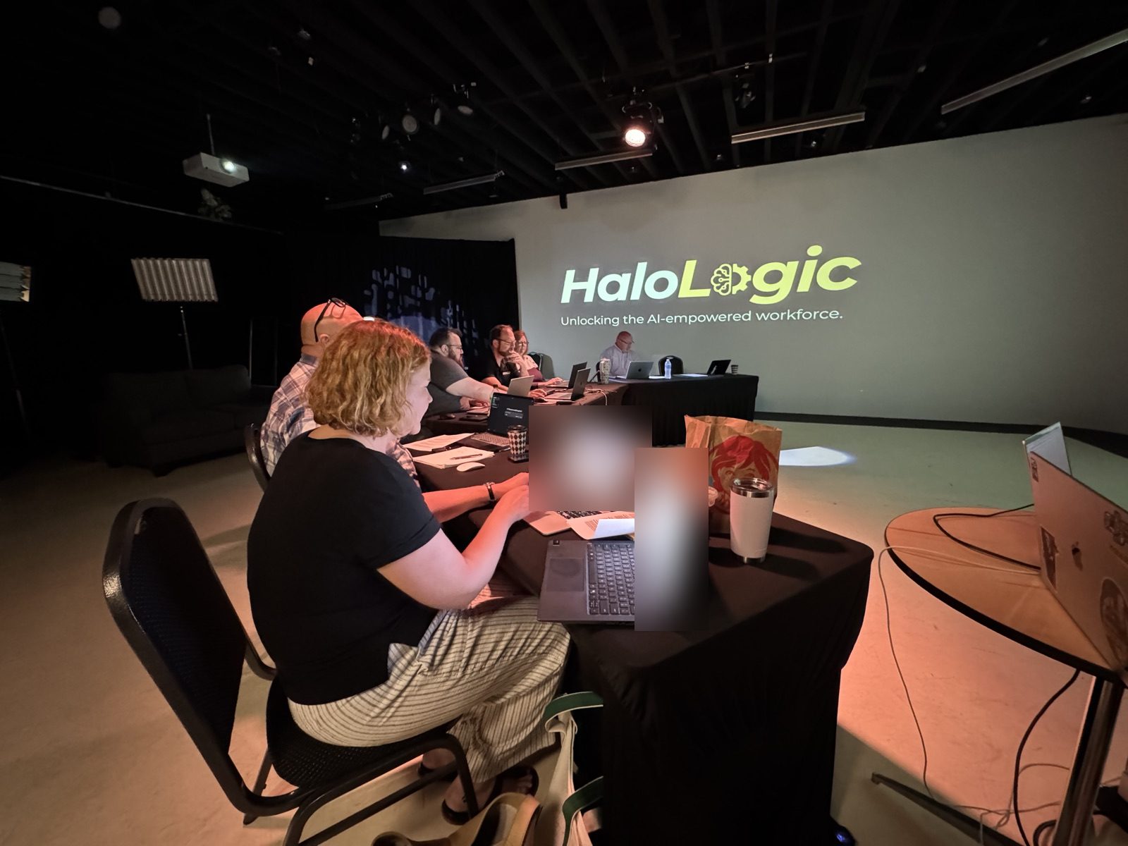 An attendee types on her laptop during the hands-on block, the Halo Logic logo projected across the studio wall.