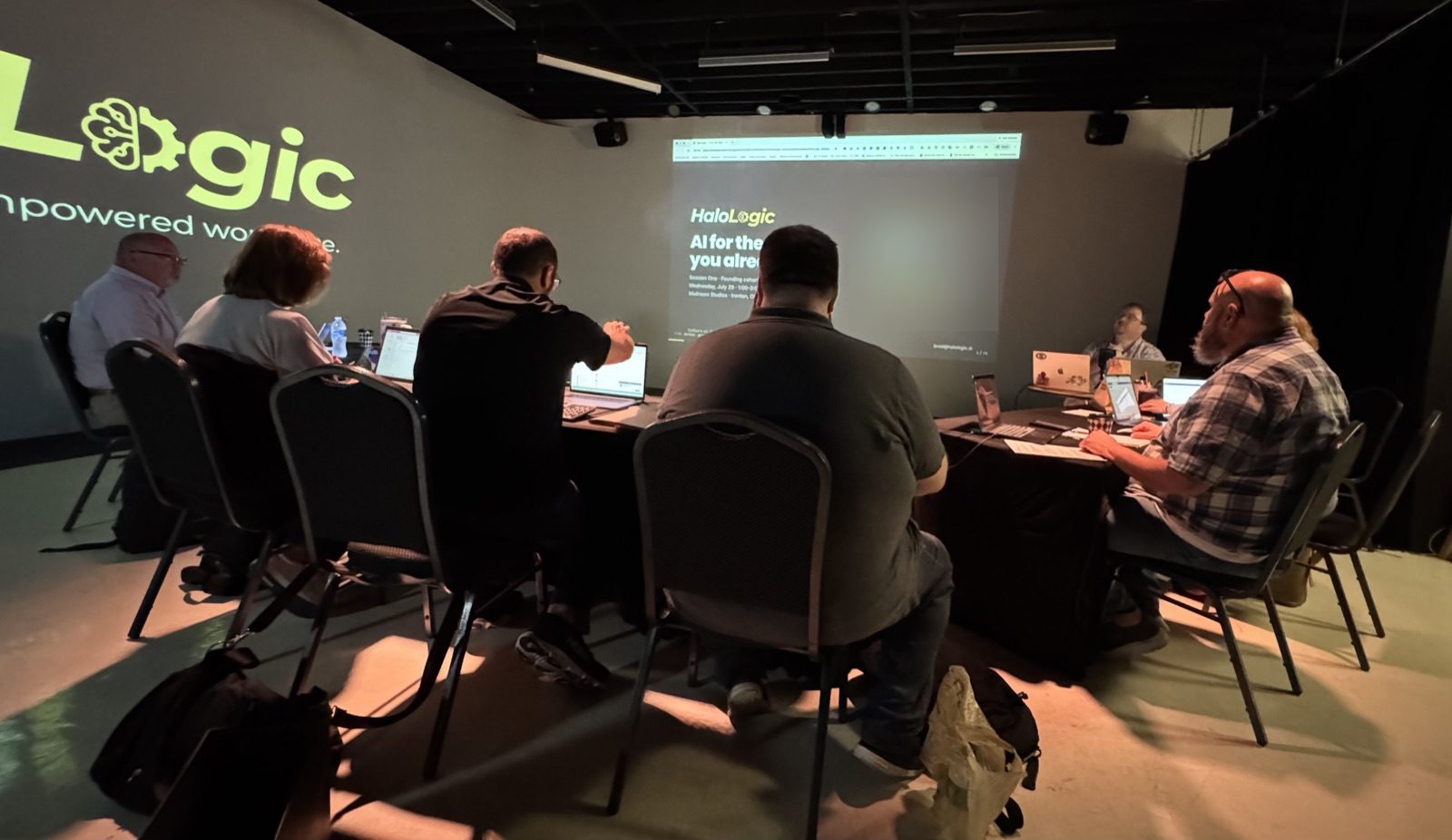 Attendees at laptops face the opening slide, AI for the work you already do, projected beside the Halo Logic logo.